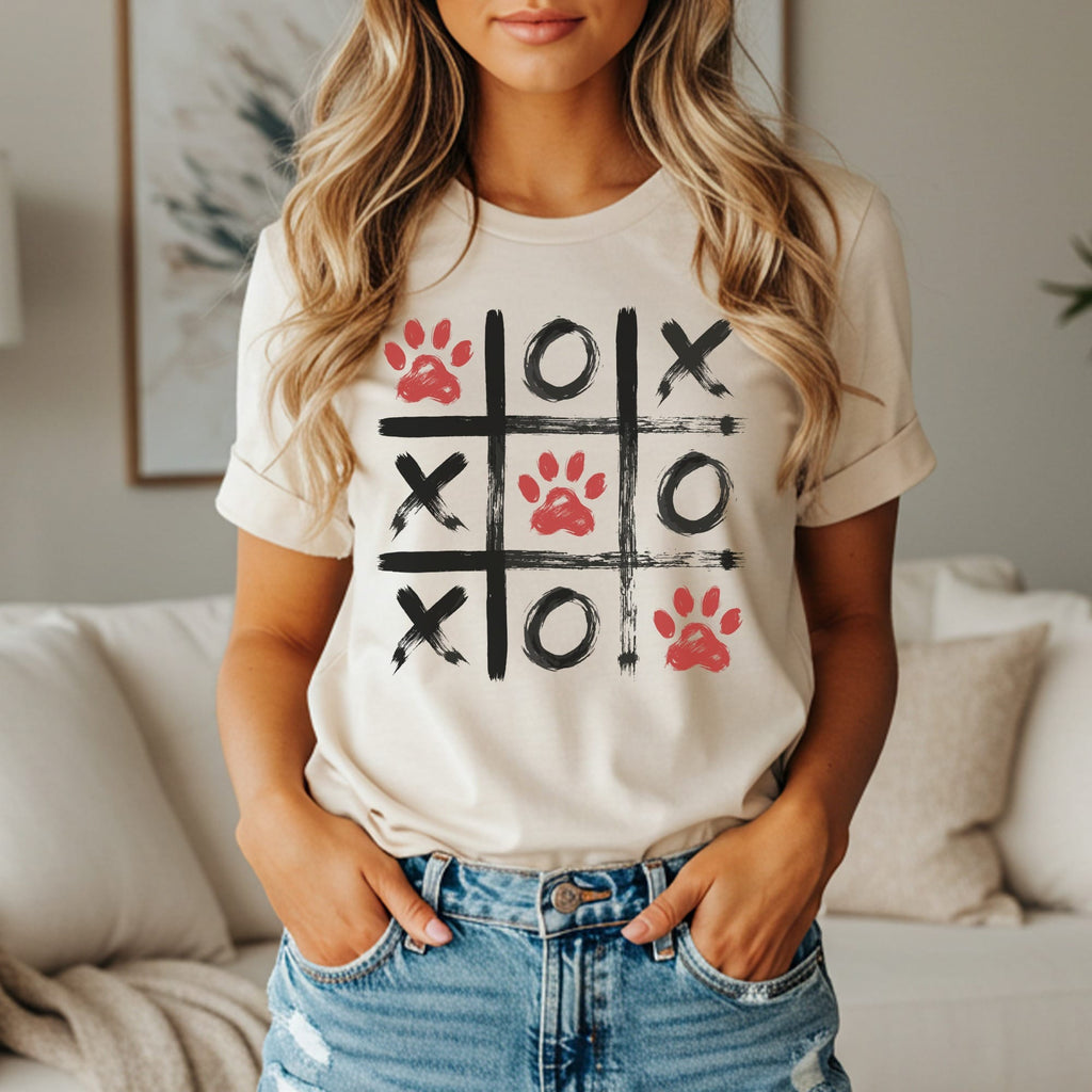 Cream t-shirt with a tic-tac-toe grid featuring red paw prints, black X's, and black O's.
