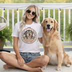 A woman wearing a white t-shirt with a dog graphic sits next to a golden retriever on a deck.