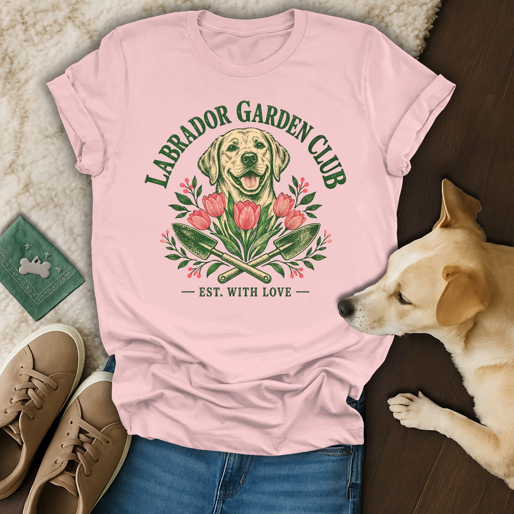 A light pink t-shirt with a green Labrador Garden Club graphic featuring a dog and tulips, laid flat with jeans, sneakers, and a real dog.
