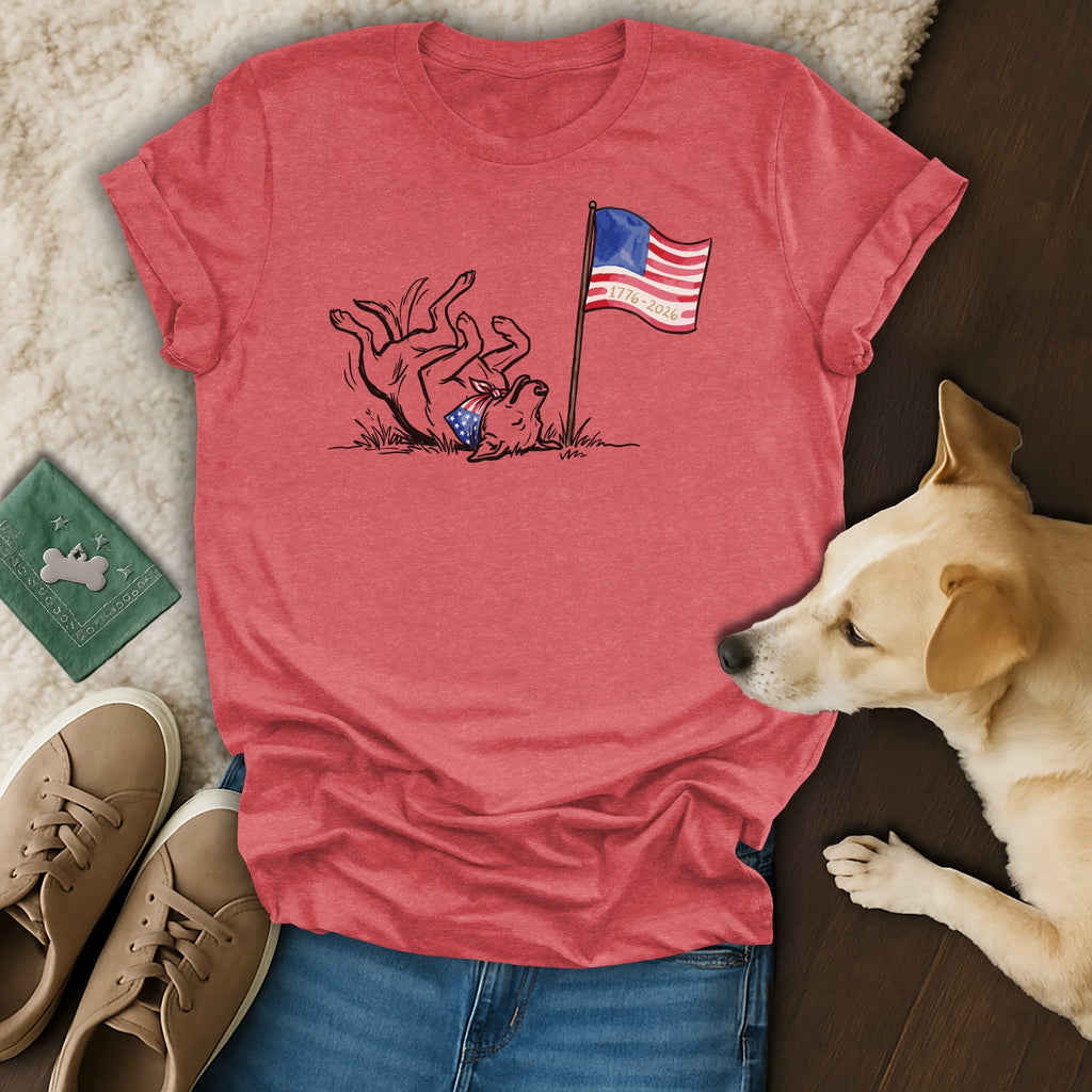Dog wearing bandana rolls playfully next to t-shirt with flag and "1776-2026".