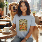 A smiling woman wearing a light blue t-shirt with a vintage seed packet graphic, sitting next to a golden retriever in a cafe.