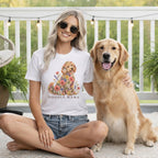 A woman wearing sunglasses and a white t-shirt featuring a floral doodle graphic sits next to a golden retriever.