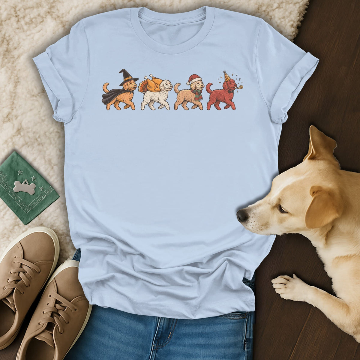 Light blue t-shirt with four cartoon dogs in holiday outfits: witch, turkey, Santa, and party hat.