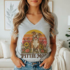 A person wearing a grey V-neck t-shirt featuring a graphic of a pit bull surrounded by flowers, a sunset background, and the text Pittie Mom.