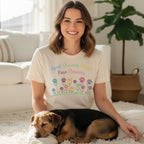 Woman wearing a cream t-shirt with "April Showers Bring Paw Flowers" and colorful paw print flowers.