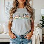 Cartoon dogs in a line wearing flower crowns and accessories on a grey t-shirt.