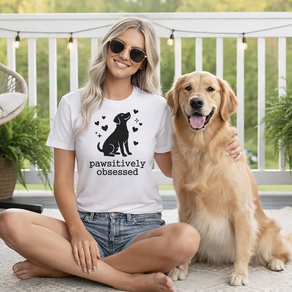 Woman wearing a white t-shirt with a dog graphic and "pawsitively obsessed" text, with a golden retriever.