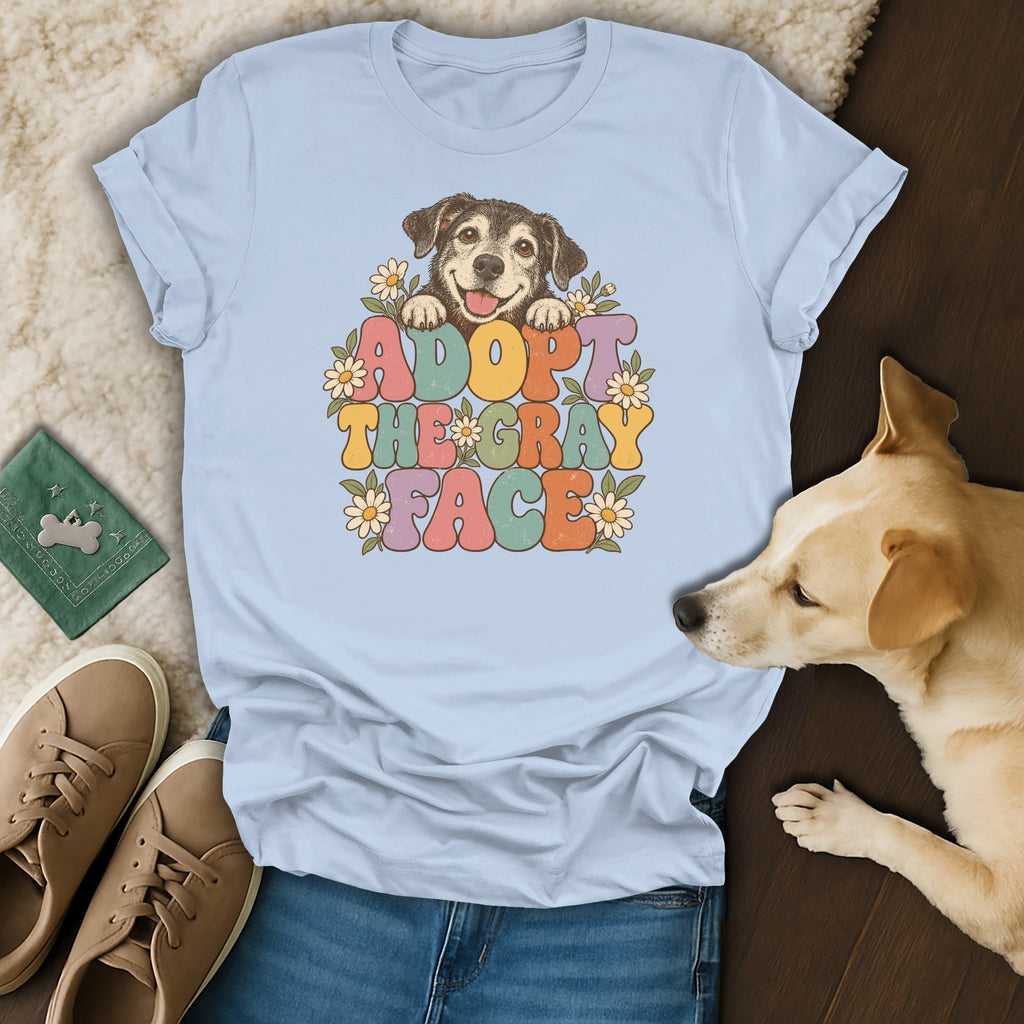 Light blue t-shirt featuring a graphic of a dog and flowers with the text Adopt the Gray Face, displayed with blue jeans, tan shoes, and a light-colored dog.