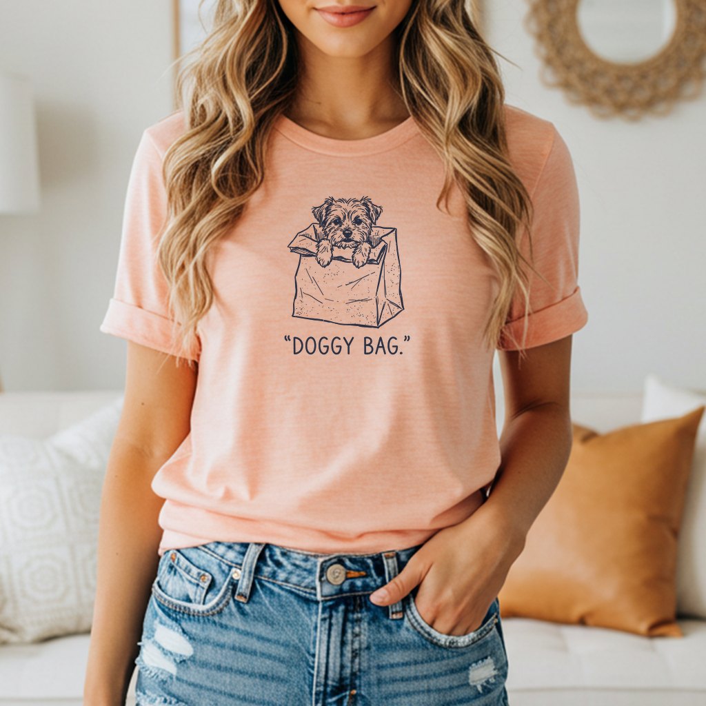 Peach t-shirt with a sketch of a dog in a paper bag and the text "DOGGY BAG."