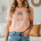 Peach t-shirt with a sketch of a dog in a paper bag and the text "DOGGY BAG."
