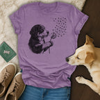 Purple t-shirt with a sketch of a puppy blowing dandelion seeds that turn into paw prints.