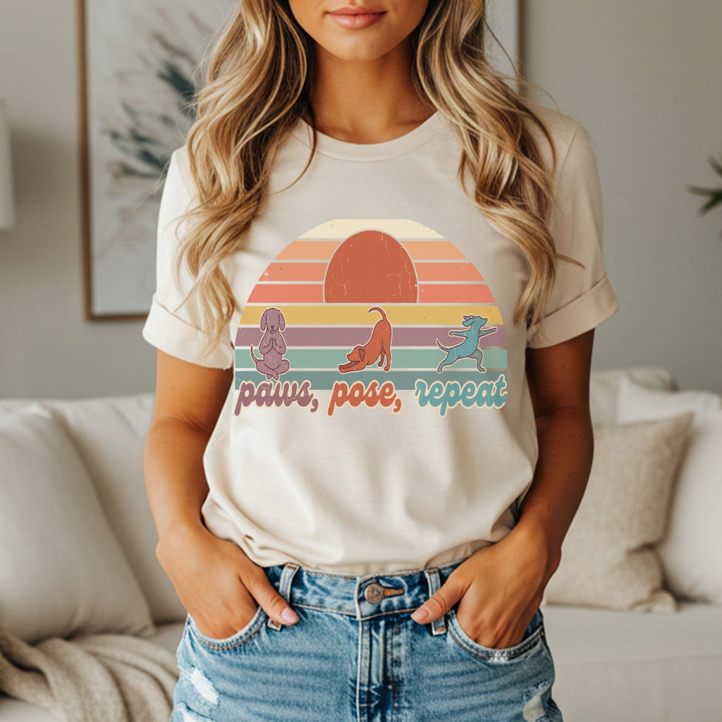 Woman wearing beige t-shirt with dogs doing yoga and text "paws, pose, repeat".