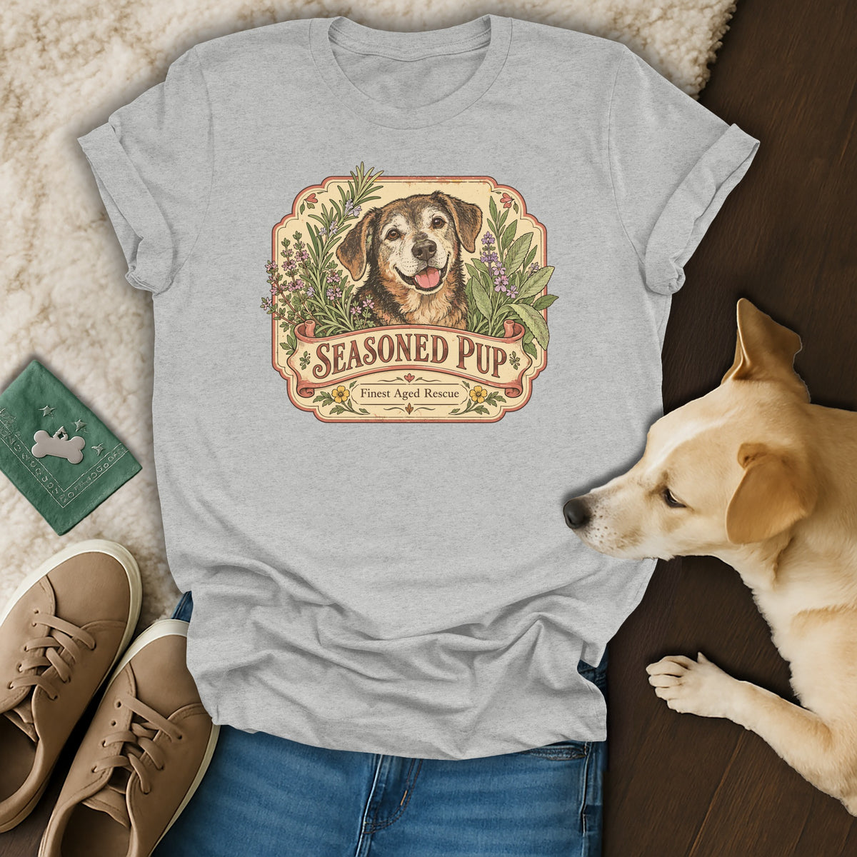 A heather gray t-shirt with a vintage "Seasoned Pup" dog and herb graphic rests on a floor.