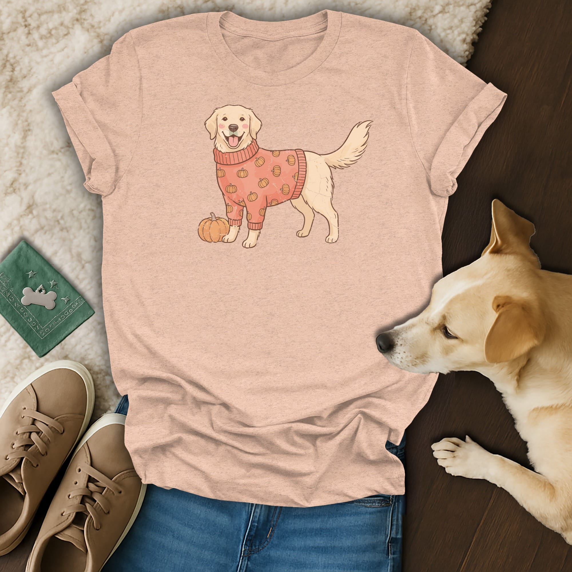 Peach t-shirt with a cartoon golden retriever wearing a pumpkin-patterned sweater and holding a pumpkin.