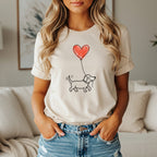 Line drawing of a dog walking with a red heart balloon on a light cream t-shirt.