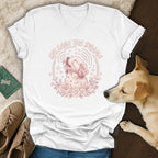 White t-shirt with a drawing of a dog howling surrounded by flowers and stars, reads "Unleash the Drama".