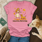 Pink t-shirt with graphic of a blonde woman and yellow dog with text "Long on love. Short on legs."