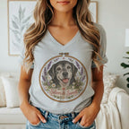 A person wearing a grey v-neck t-shirt featuring an embroidered hoop graphic of a dog surrounded by flowers and the text Silver & Sweet.