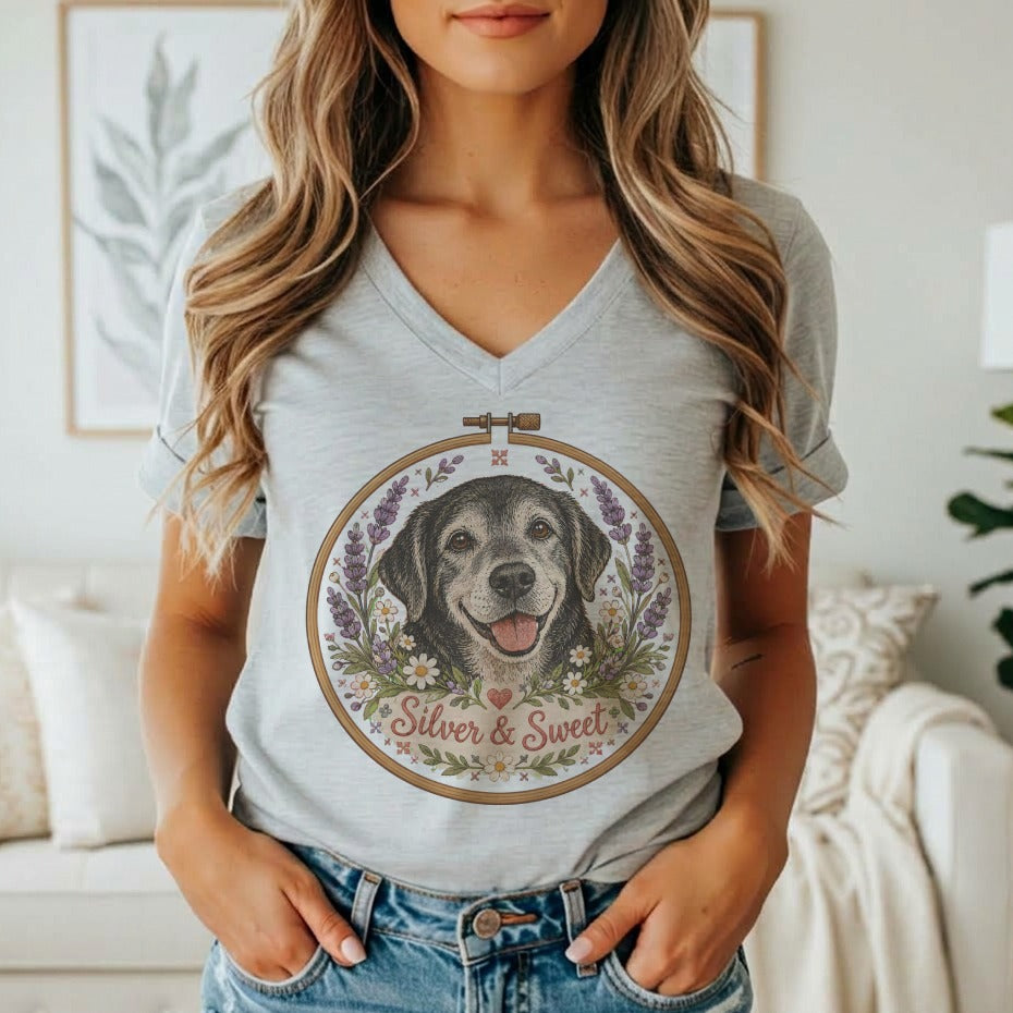 A person wearing a grey v-neck t-shirt featuring an embroidered hoop graphic of a dog surrounded by flowers and the text Silver & Sweet.