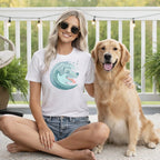 Woman in white t-shirt with wave dog graphic sits with a golden retriever.
