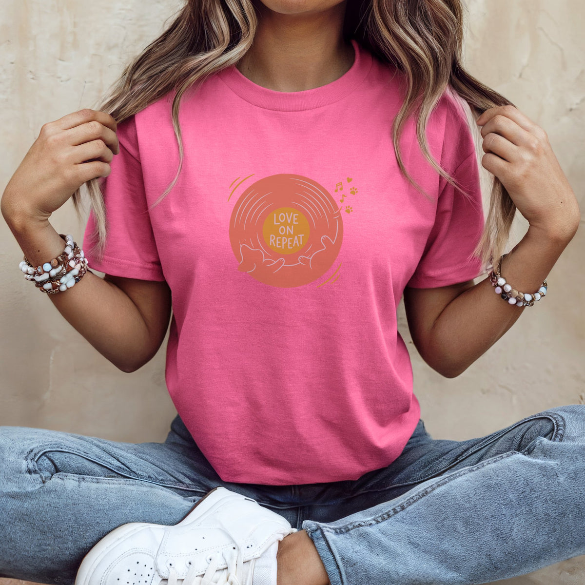 A person wearing a bright pink t-shirt with a vinyl record graphic that reads Love on Repeat.