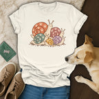 Cream t-shirt featuring a colorful illustration of snails with pawprint shells, displayed with shoes and a dog.