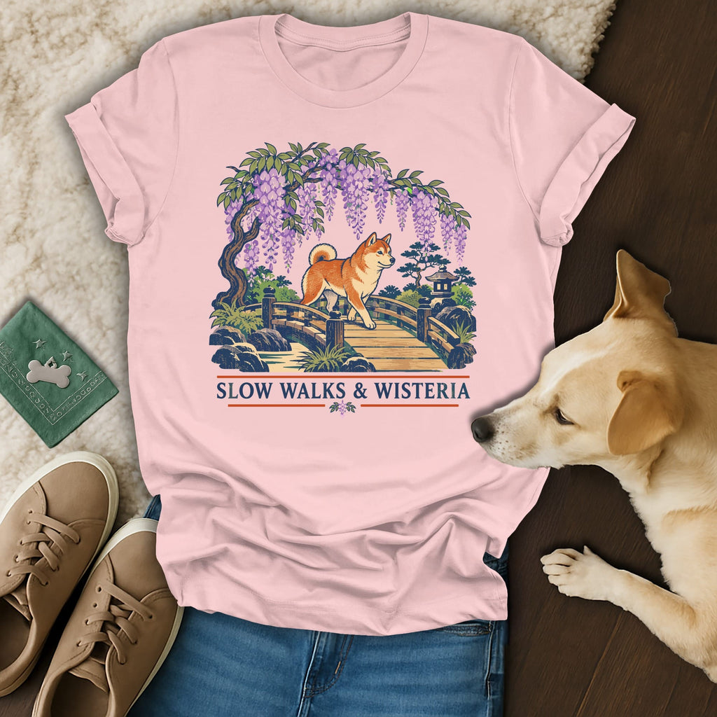 Light pink t-shirt featuring a Japanese-style graphic of a Shiba Inu crossing a bridge under wisteria blossoms, with text reading Slow Walks & Wisteria.