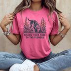 A woman wearing a pink t-shirt with a basset hound graphic and the text Follow Your Nose to the Flowers.