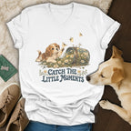 A white V-neck t-shirt featuring a vintage graphic of a puppy, flowers, and the text Catch The Little Moments.