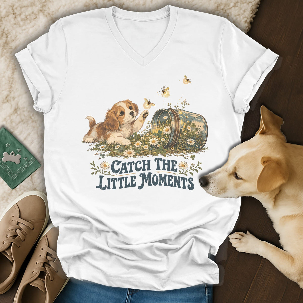 A white V-neck t-shirt featuring a vintage graphic of a puppy, flowers, and the text Catch The Little Moments.