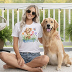 Woman wearing white t-shirt with graphic of a dog in a garden, sitting with a golden retriever.