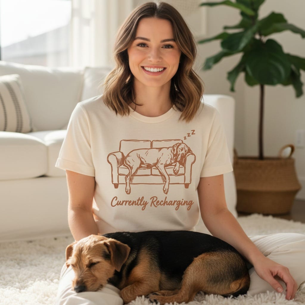Woman wearing cream t-shirt with dog sleeping graphic, sitting with dog.