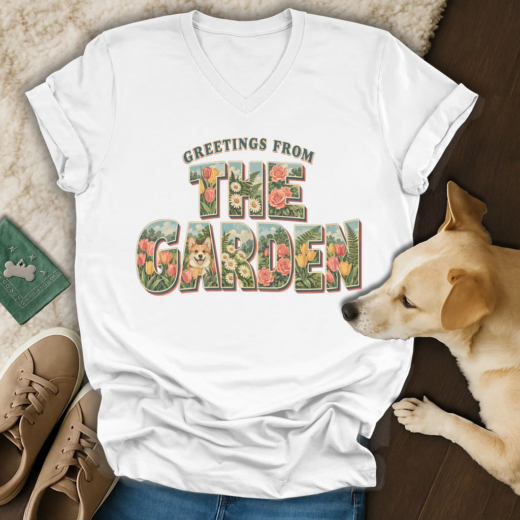A white V-neck t-shirt with a vintage garden graphic and dog illustration, resting near a small dog.