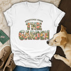 A white V-neck t-shirt with a vintage garden graphic and dog illustration, resting near a small dog.