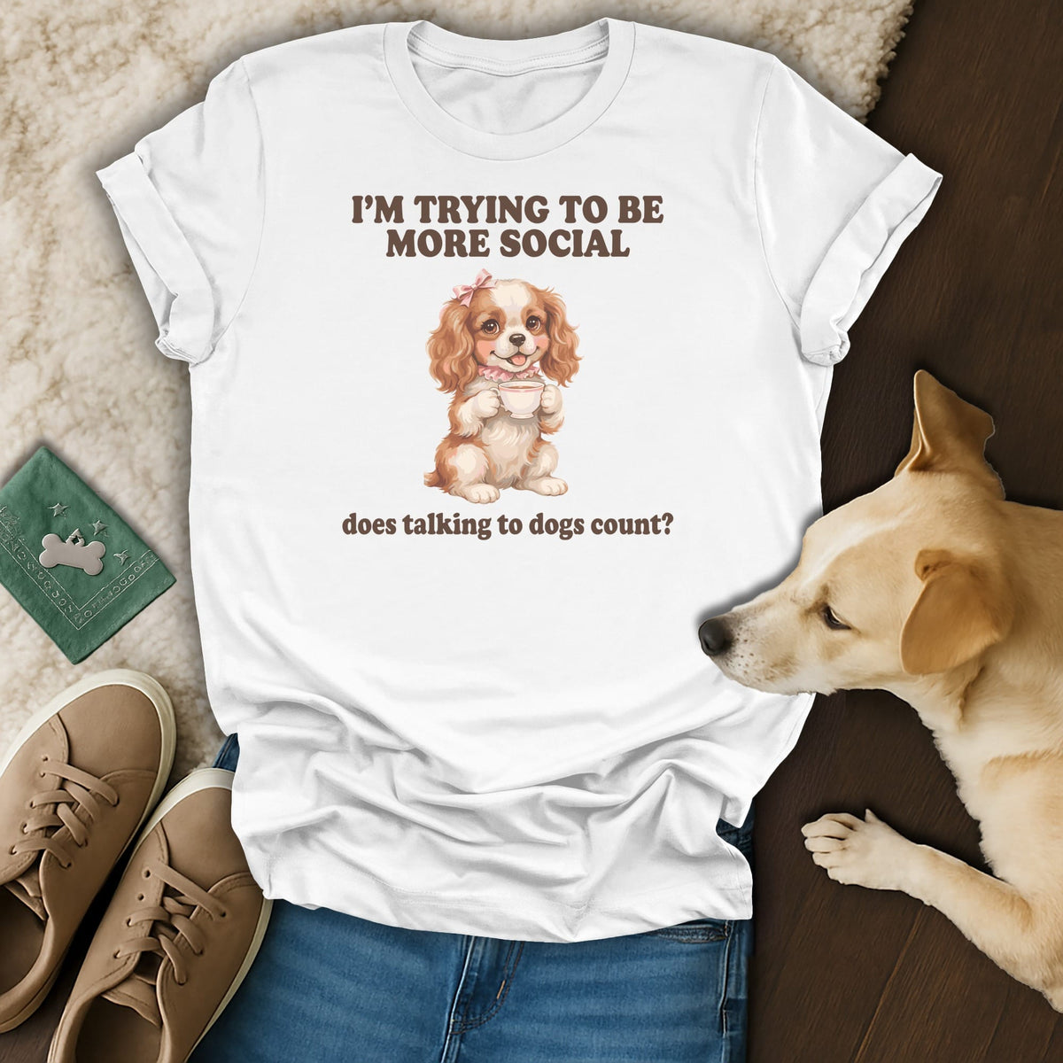 White t-shirt with a drawing of a dog holding a cup, text says "I'M TRYING TO BE MORE SOCIAL does talking to dogs count?"