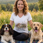 A smiling woman wearing a white t-shirt with a puppy graphic, flanked by two dogs in a grassy field.