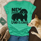 Green t-shirt with black graphic of a shaggy dog and text "NEW FOUND LAND ON THE COUCH".