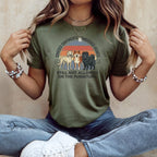 Green t-shirt with three dogs and sunset graphic; text reads "Crossed Continents, Conquered Hearts, Still Not Allowed on the Furniture."