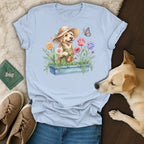 T-shirt graphic of a golden retriever wearing a straw hat and overalls watering flowers.
