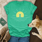 Turquoise t-shirt with a minimalist dog silhouette against a yellow sun and ocean waves.