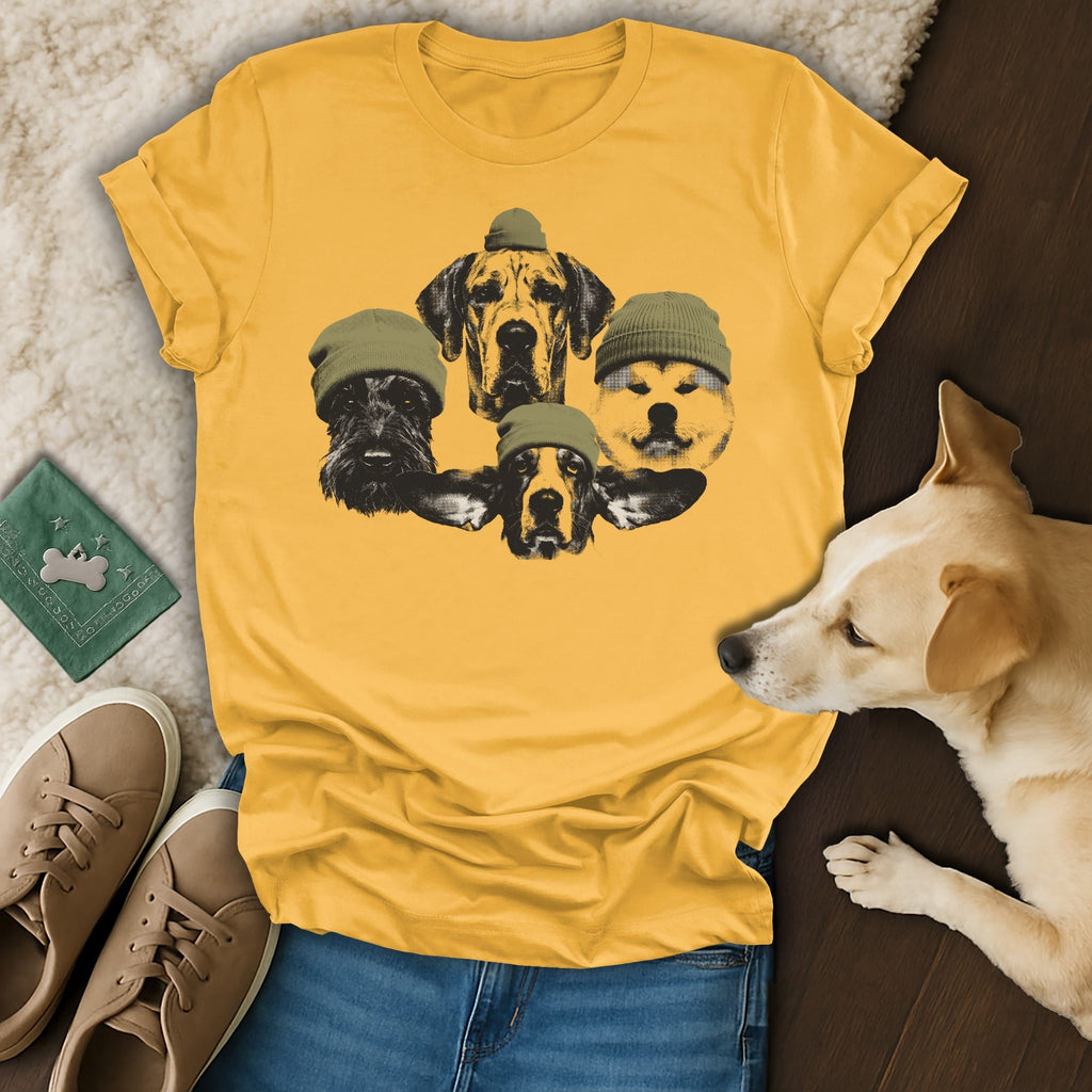 T-shirt with five dog heads wearing green beanies, against a wood and fluffy background.