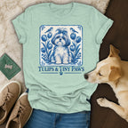 A light green t-shirt features a blue and white Delft-style dog graphic with tulips, birds, and text.