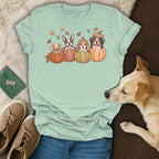 Four cartoon dogs in pumpkins with fall leaves on a light green t-shirt.