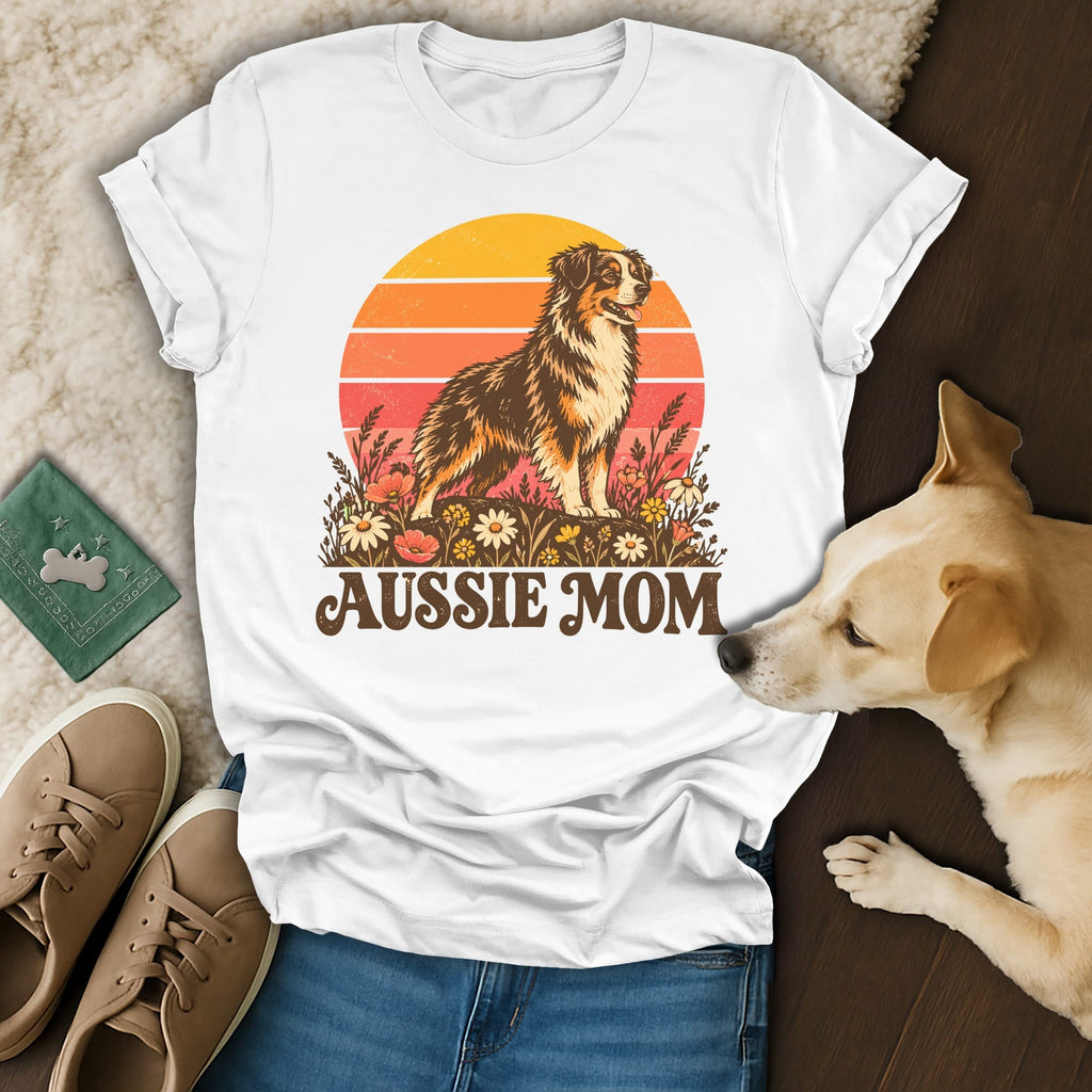 White t-shirt with an Aussie Mom graphic featuring an Australian Shepherd in front of a sunset, surrounded by flowers.