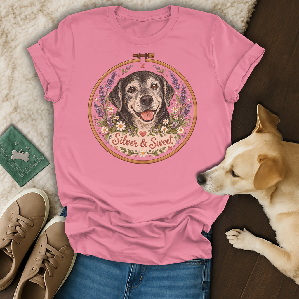 A pink t-shirt featuring an embroidered-style illustration of a happy dog framed by flowers, with the text "Silver & Sweet".