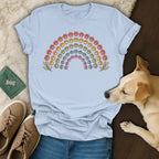 Light blue t-shirt featuring a colorful rainbow made of paw prints, laid out with a dog and sneakers.