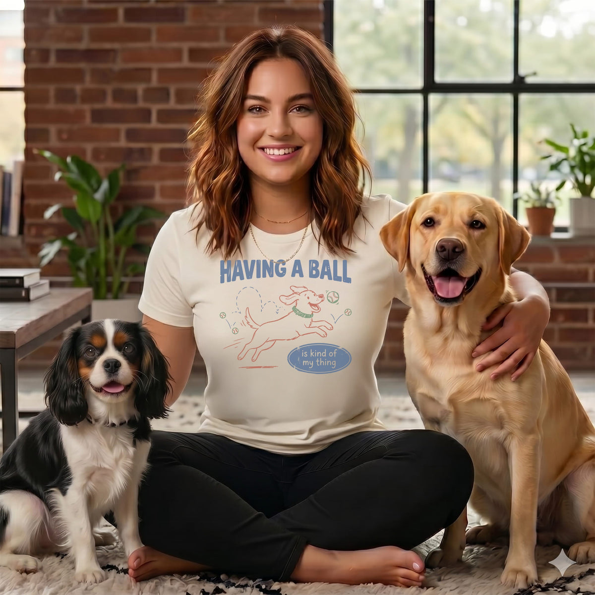 Woman with two dogs wearing a shirt with "Having a ball is kind of my thing" graphic.