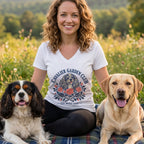 A smiling woman wearing a Cavalier Garden Club t-shirt poses outdoors with two dogs.