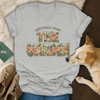 Heather gray v-neck t-shirt featuring a vintage floral graphic with text reading Greetings from the Garden, surrounded by a dog and shoes.