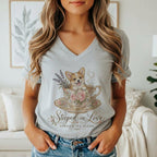 A woman wearing a gray V-neck t-shirt featuring a cartoon corgi inside a floral teacup.